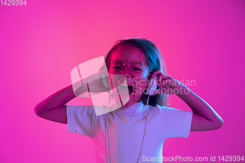 Image of Portrait of little girl in headphones on purple gradient background in neon light