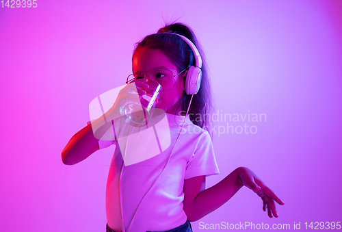 Image of Portrait of little girl in headphones on purple gradient background in neon light