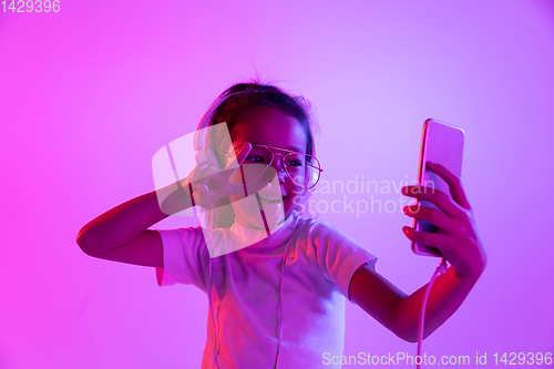 Image of Portrait of little girl in headphones on purple gradient background in neon light
