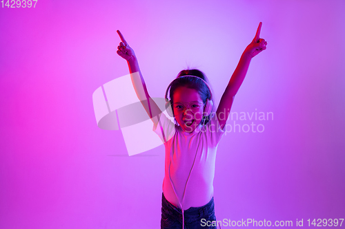 Image of Portrait of little girl in headphones on purple gradient background in neon light