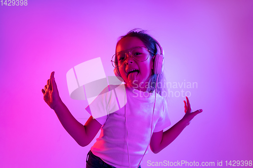 Image of Portrait of little girl in headphones on purple gradient background in neon light