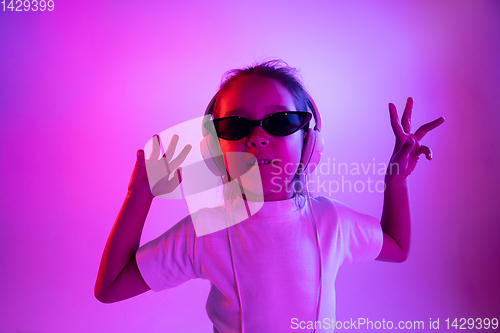 Image of Portrait of little girl in headphones on purple gradient background in neon light