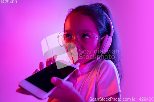 Image of Portrait of little girl in headphones on purple gradient background in neon light