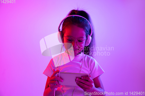 Image of Portrait of little girl in headphones on purple gradient background in neon light