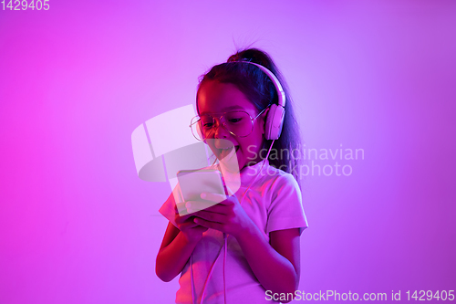 Image of Portrait of little girl in headphones on purple gradient background in neon light