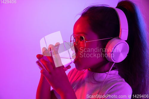 Image of Portrait of little girl in headphones on purple gradient background in neon light