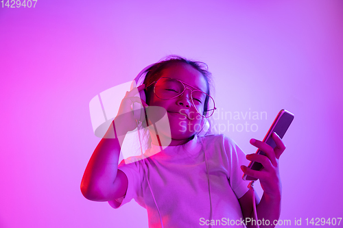 Image of Portrait of little girl in headphones on purple gradient background in neon light