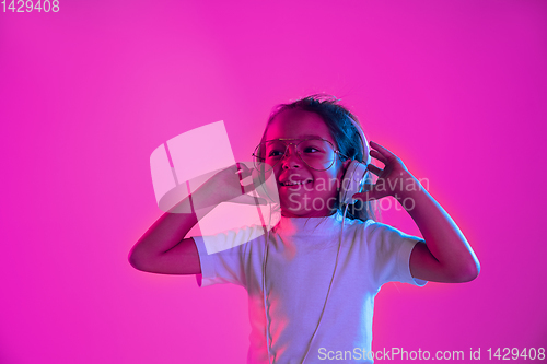 Image of Portrait of little girl in headphones on purple gradient background in neon light