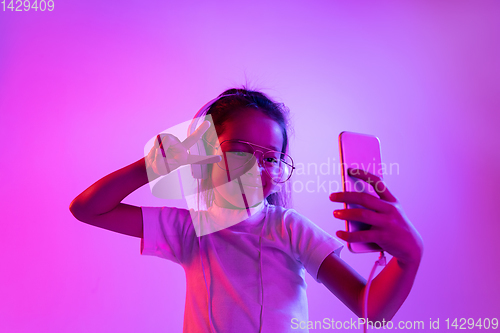 Image of Portrait of little girl in headphones on purple gradient background in neon light