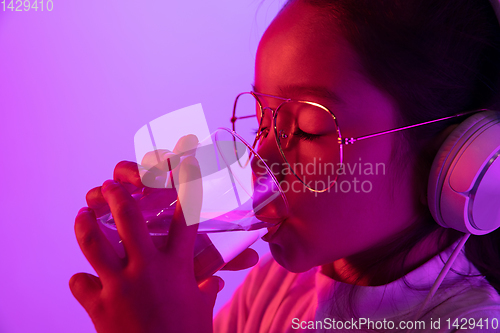 Image of Portrait of little girl in headphones on purple gradient background in neon light