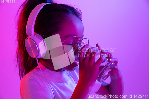 Image of Portrait of little girl in headphones on purple gradient background in neon light