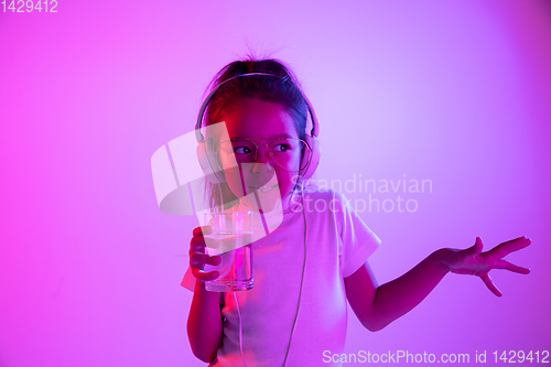 Image of Portrait of little girl in headphones on purple gradient background in neon light