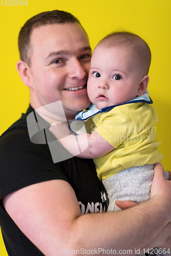 Image of portrait of happy young father holding baby isolated on yellow