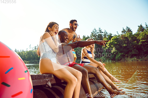 Image of Group of happy friends having fun while sitting and laughting on the pier on river