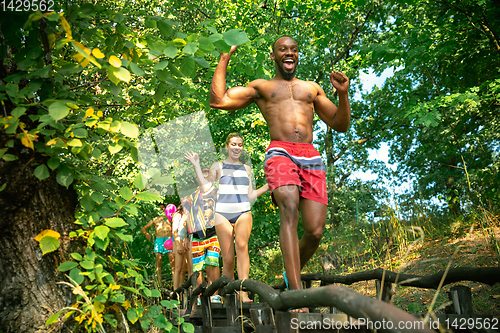 Image of Group of happy friends having fun while running to swim on river