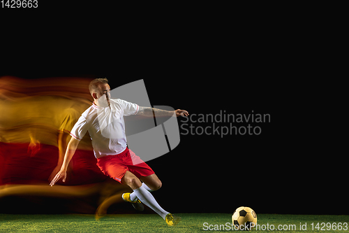 Image of Male soccer player kicking ball on dark background in mixed light