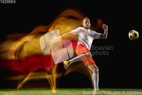 Image of Male soccer player kicking ball on dark background in mixed light