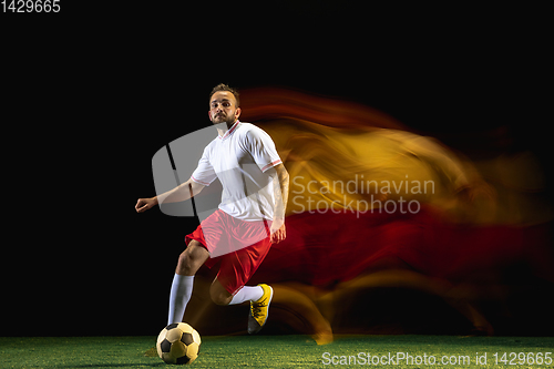 Image of Male soccer player kicking ball on dark background in mixed light