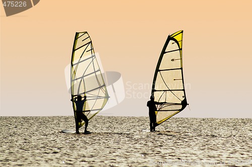 Image of Silhouettes of two windsurfers on waves of a gulf 