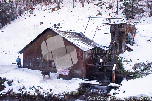 Image of confident senior blacksmith in front of watermill