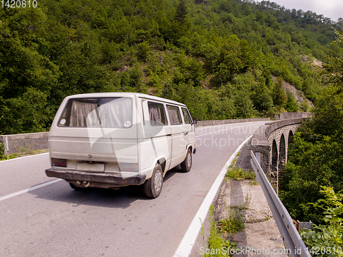 Image of old white van on asphalt road in beautiful countryside