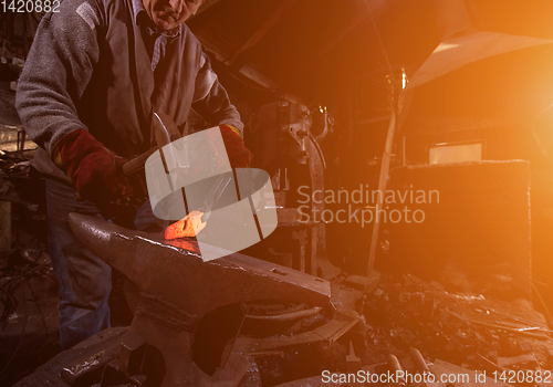 Image of blacksmith manually forging the molten metal with sunlight throu