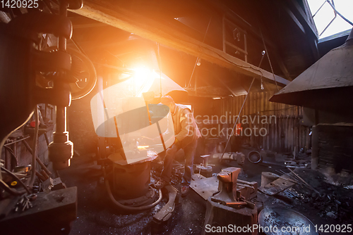 Image of blacksmith manually forging the molten metal with sunlight throu