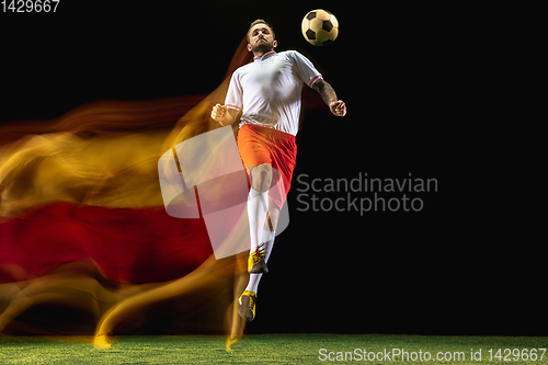 Image of Male soccer player kicking ball on dark background in mixed light