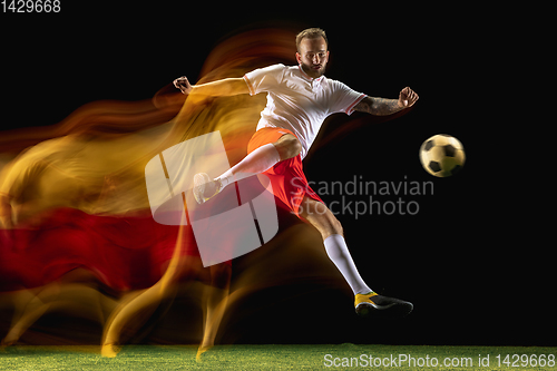 Image of Male soccer player kicking ball on dark background in mixed light