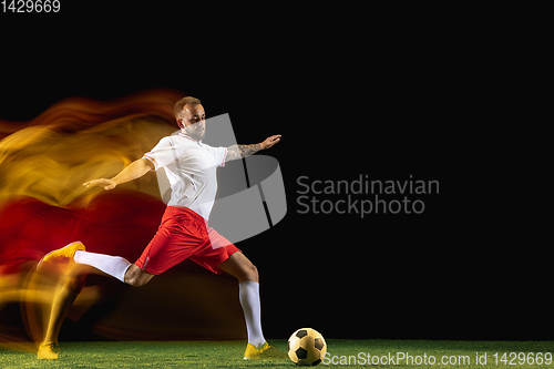 Image of Male soccer player kicking ball on dark background in mixed light