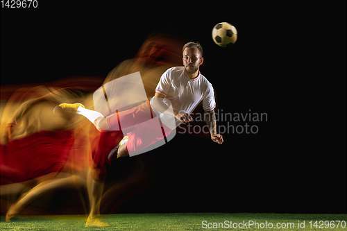 Image of Male soccer player kicking ball on dark background in mixed light