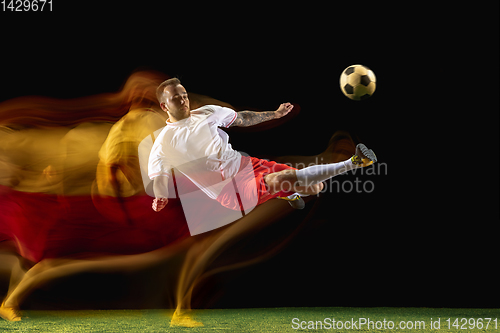 Image of Male soccer player kicking ball on dark background in mixed light