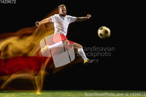 Image of Male soccer player kicking ball on dark background in mixed light