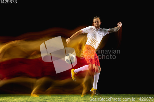 Image of Male soccer player kicking ball on dark background in mixed light