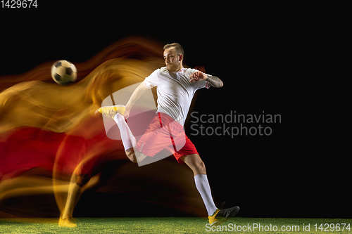 Image of Male soccer player kicking ball on dark background in mixed light