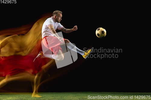 Image of Male soccer player kicking ball on dark background in mixed light