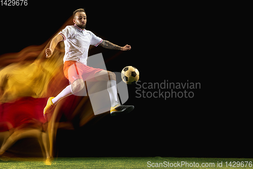 Image of Male soccer player kicking ball on dark background in mixed light