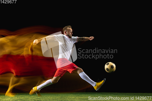 Image of Male soccer player kicking ball on dark background in mixed light