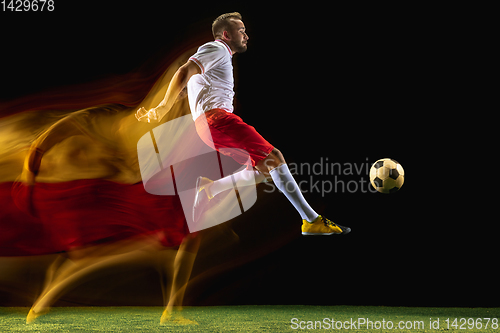 Image of Male soccer player kicking ball on dark background in mixed light