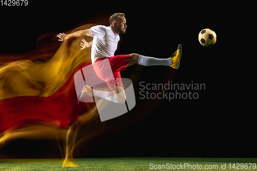 Image of Male soccer player kicking ball on dark background in mixed light