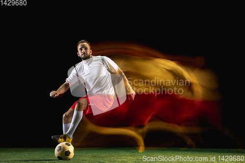 Image of Male soccer player kicking ball on dark background in mixed light