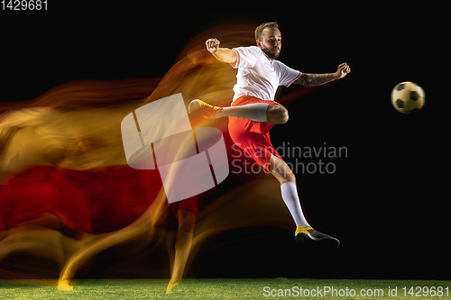 Image of Male soccer player kicking ball on dark background in mixed light