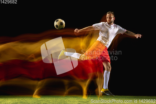 Image of Male soccer player kicking ball on dark background in mixed light