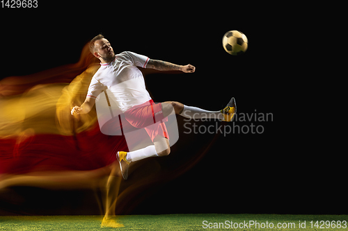 Image of Male soccer player kicking ball on dark background in mixed light