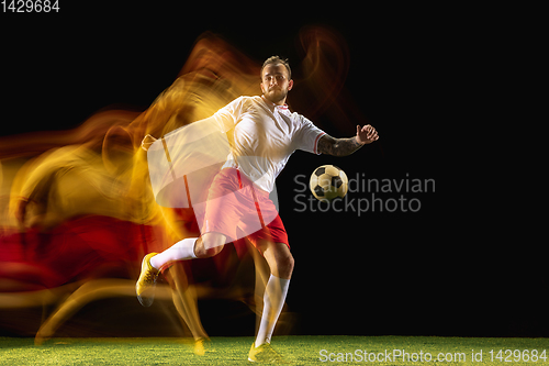 Image of Male soccer player kicking ball on dark background in mixed light