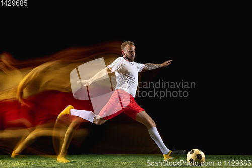 Image of Male soccer player kicking ball on dark background in mixed light