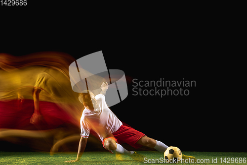 Image of Male soccer player kicking ball on dark background in mixed light