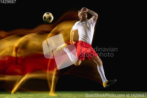 Image of Male soccer player kicking ball on dark background in mixed light