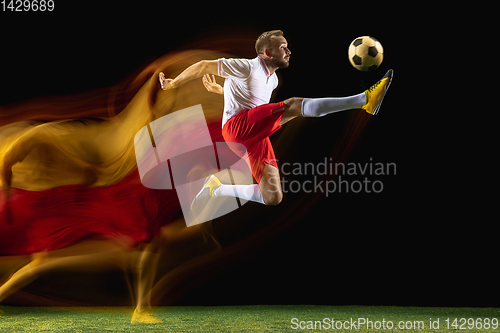 Image of Male soccer player kicking ball on dark background in mixed light