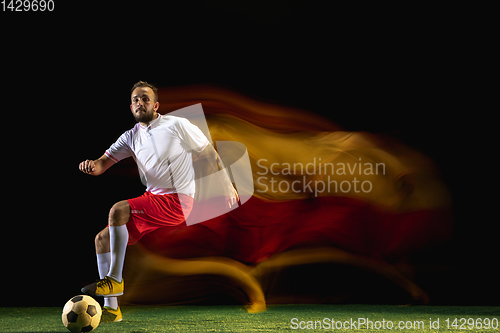 Image of Male soccer player kicking ball on dark background in mixed light